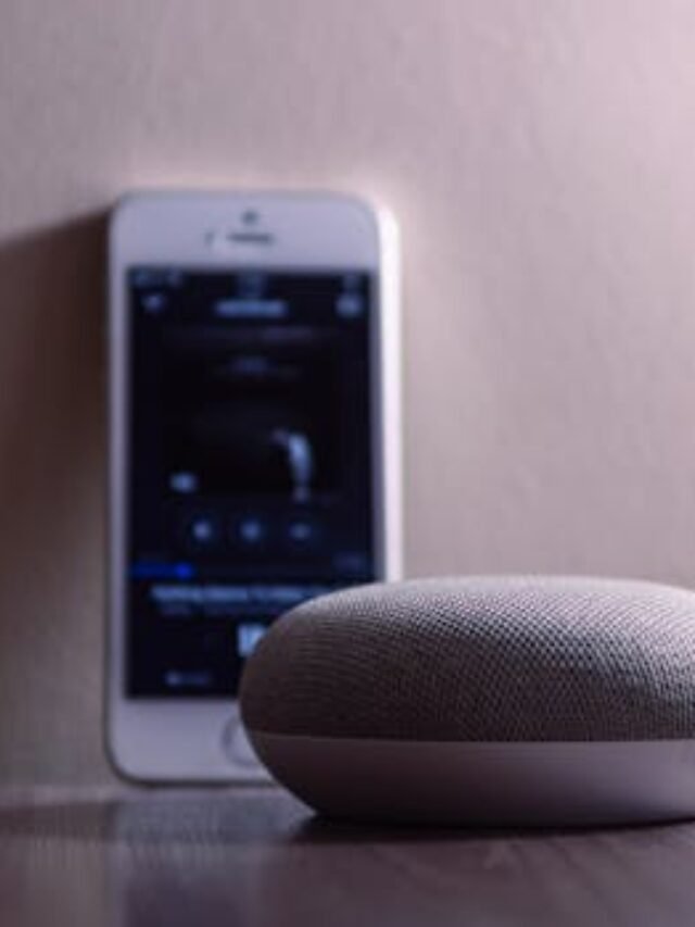 A modern smart speaker and smartphone on a wooden table, indoors.