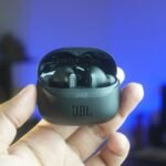 High-quality close-up of hand holding JBL wireless earbuds indoors with cozy background lighting.