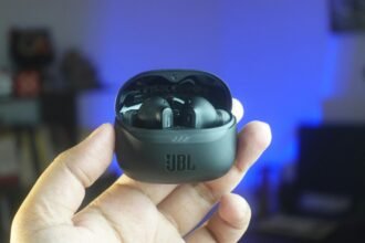 High-quality close-up of hand holding JBL wireless earbuds indoors with cozy background lighting.