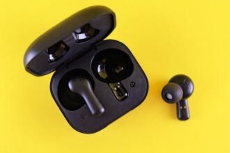 Close-up of black wireless earbuds and charging case on a vibrant yellow background.