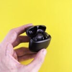 Close-up of a hand holding black wireless Bluetooth earbuds with a yellow backdrop.
